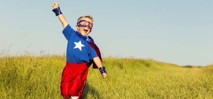 young boy with a superhero costume playing in a field