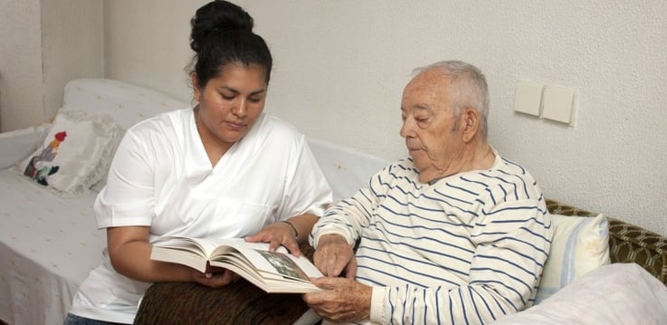senior care nurse sitting with a male resident and reading him a book