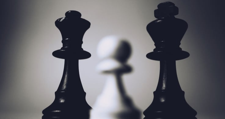 closeup of chess pieces: a white pawn and a black king and queen