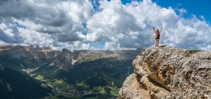mountain climber on top of a plateau, overlooking a valley, with hands raised in triumph
