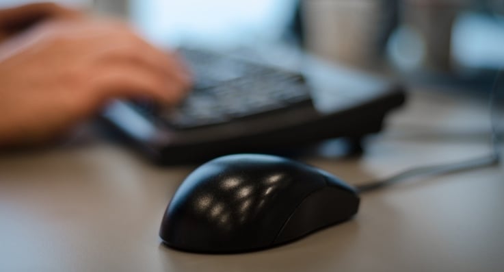 closeup of hands typing on a keyboard with a computer mouse in the foreground