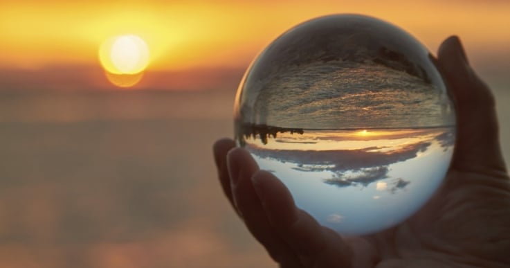 hand holding a glass ball with a beach and sunset in the background