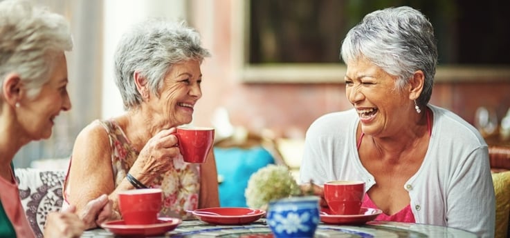 3 female long-term care residents laugh while drinking tea at a dining table
